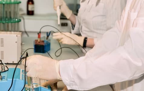 Two laboratory assistants carry out electrolysis process, adding reagents for science research