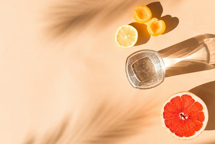 cool water in glas and fruits on beige background in sunlight flat lay