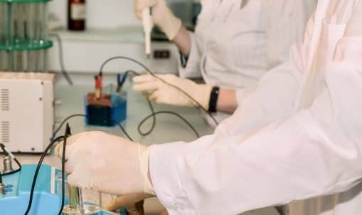 Two laboratory assistants carry out electrolysis process, adding reagents for science research